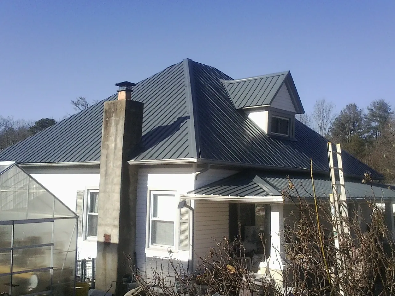 Dark blue standing seam metal roof on a white farmhouse with dormer — Slate & Tile Roof Repair by Roofing Brothers in Briggsdale