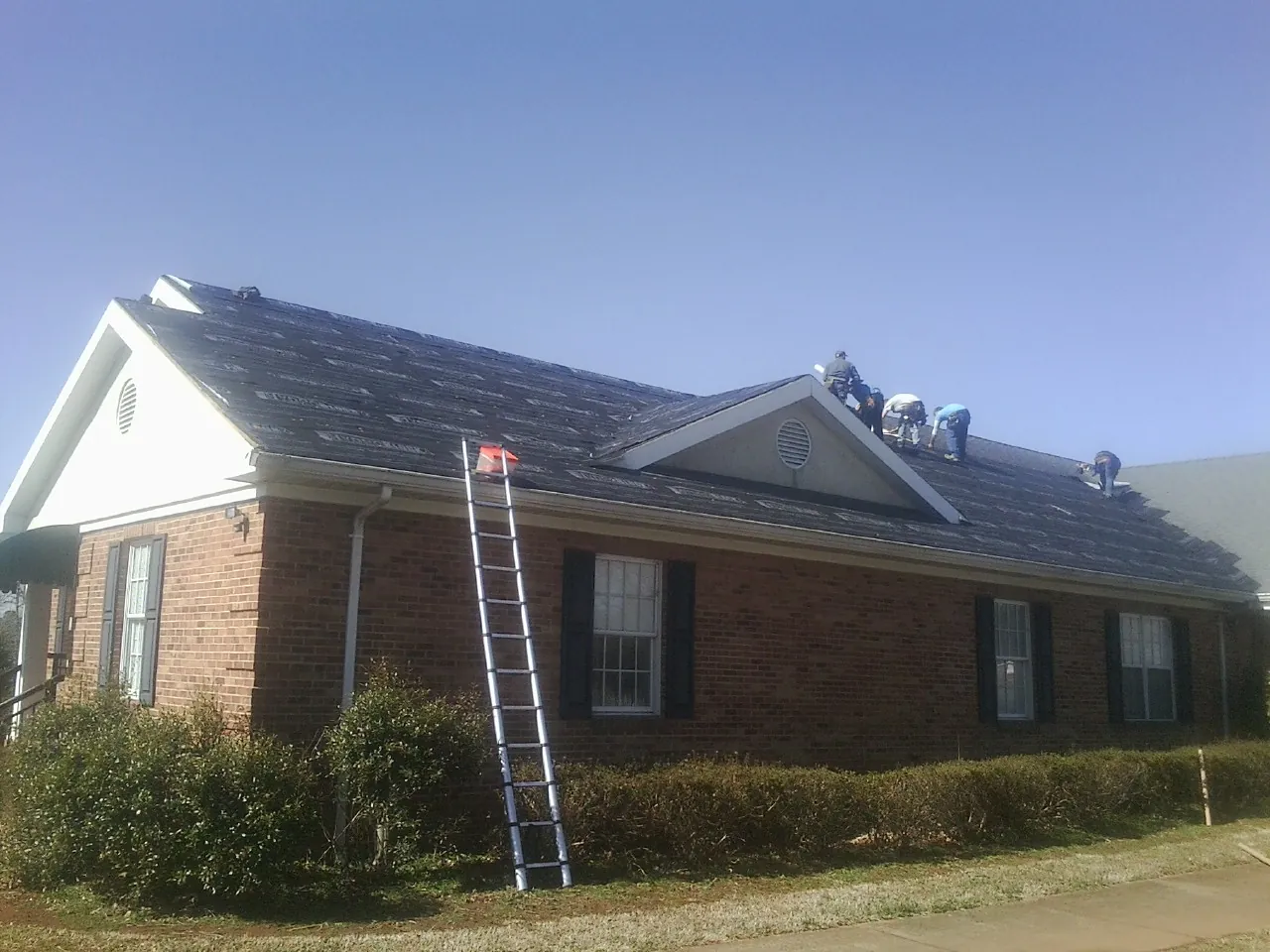 Crew tearing shingles off a brick ranch roof with a ladder set — Emergency Roof Repair work by our crew in Briggsdale