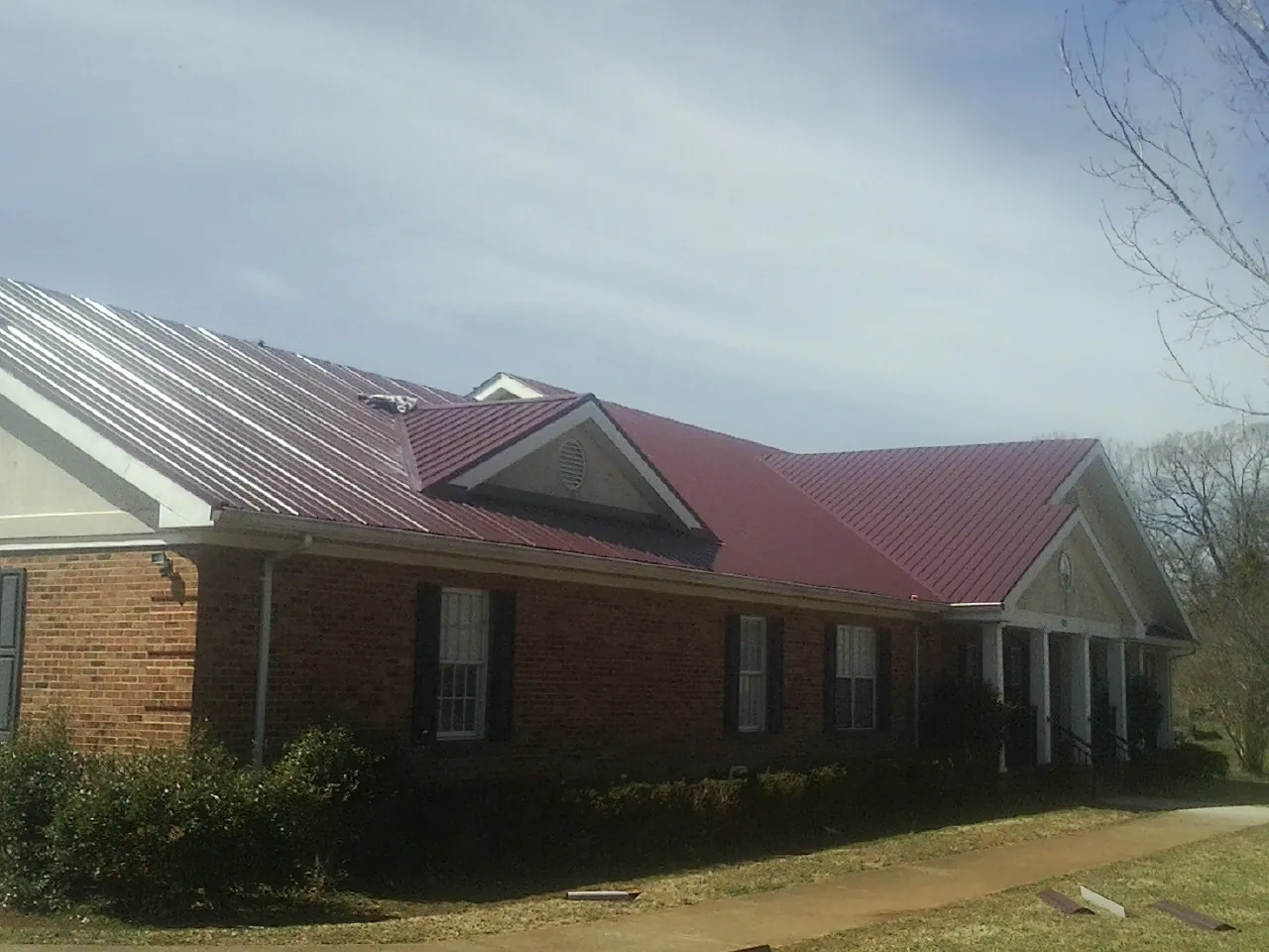 Red metal roof with gabled entries on a long brick building, from a Hail Damage Roof Repair job in Briggsdale
