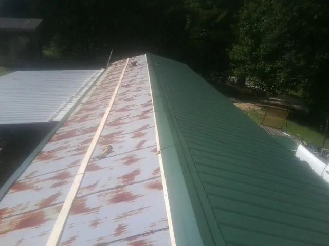 Old rusted panels beside newly installed green metal roofing — Wind Damage Roof Repair by Roofing Brothers in Briggsdale
