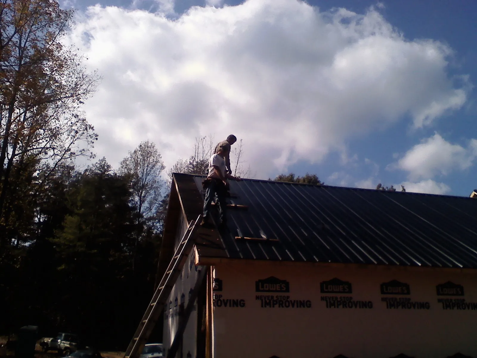 Roofer fastening dark metal panels high against a cloudy sky, from a Roof Inspection job in Briggsdale