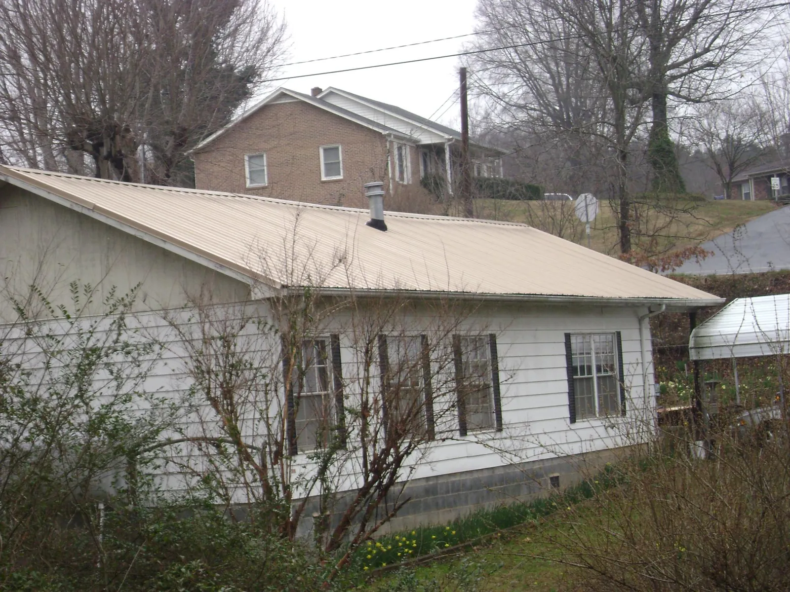 Tan metal roof on a white sided house set into a hillside — Commercial Roofing by Roofing Brothers in Briggsdale