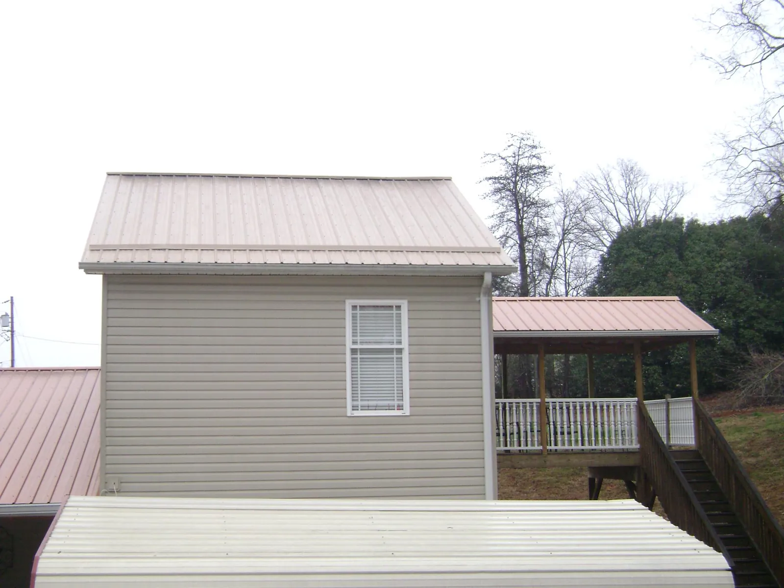 Tan metal roofs on a two story addition and attached porch, from a Roof Replacement job in Briggsdale
