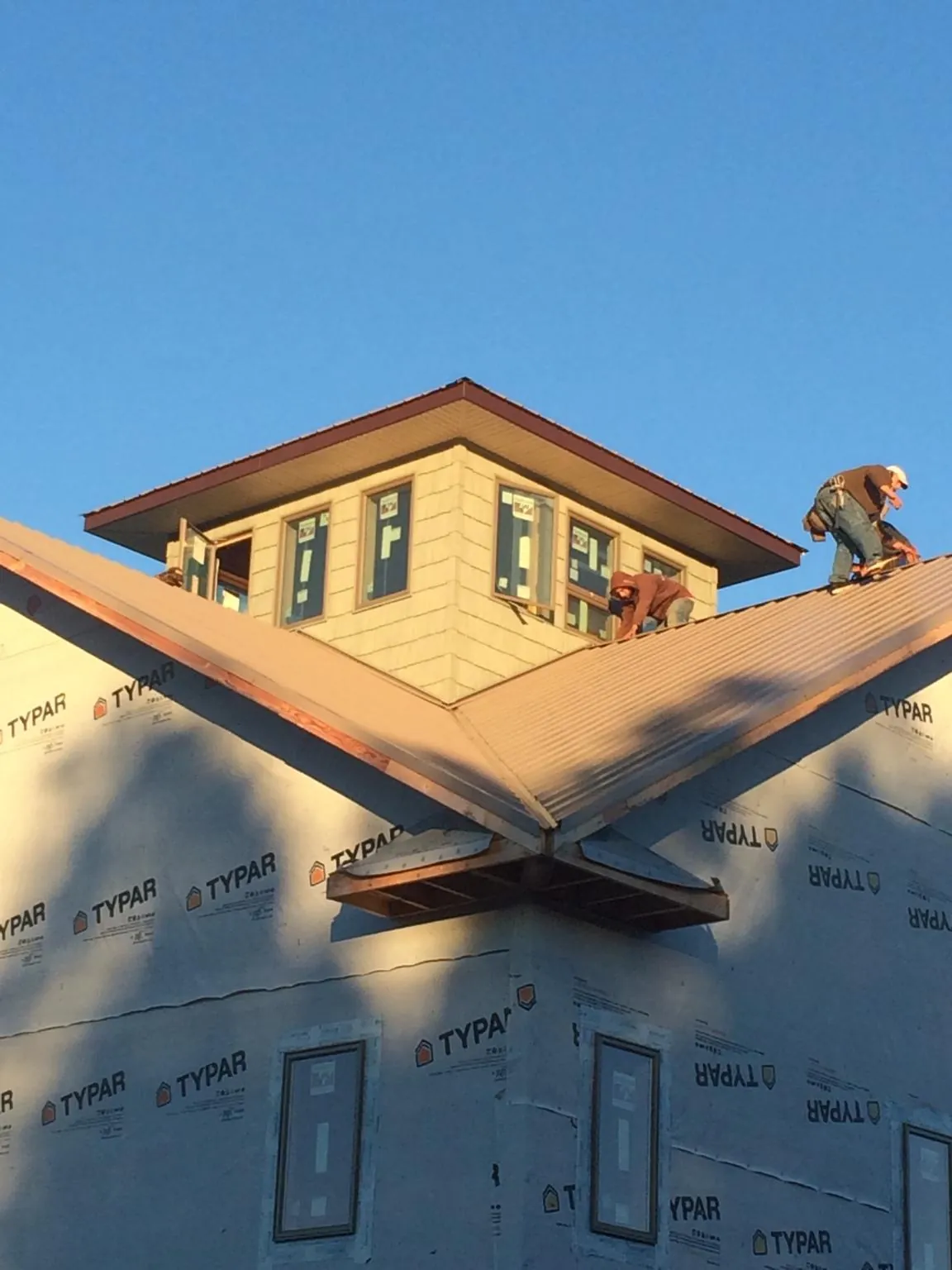 Roofers working around a rooftop cupola on a new metal roof at sunset — Roof Waterproofing in Briggsdale by Roofing Brothers